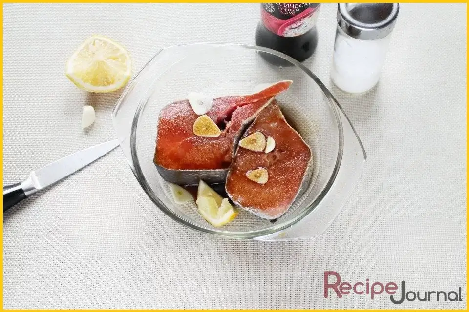 Чеснок нарезать тонкими пластинами добавить к рыбе, посолить, сбрызнуть лимонным соком, добавить соевый соус. Посолить, хорошо обмакнуть стейки в маринад и отставить на 10-15 минут.