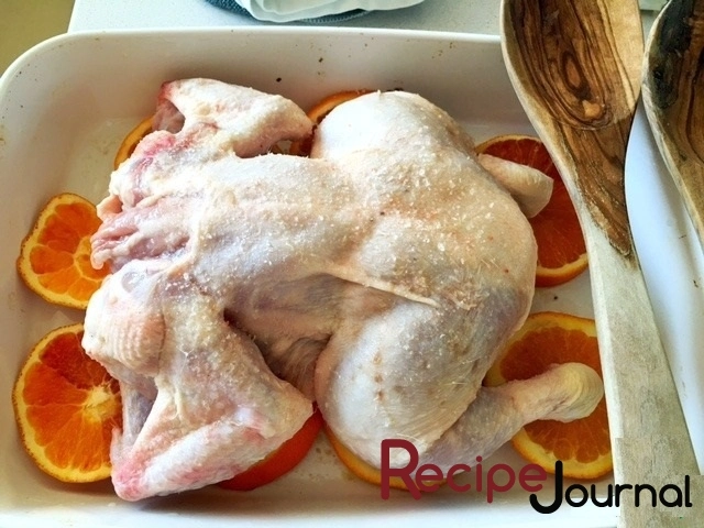 Курицу обтираем сухой салфеткой ( по последним рекомендациям мыть не советуют), натираем солью и перцем и, разрезав посередине, выкладываем на апельсины.