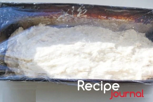 Форму для запекания смазать маслом или застелить промасленной пекарской бумагой и переложить в неё тесто. Распределить как можно более равномерно и накрыть пищевой пленкой. Отставить для подъема  в теплое место при комнатной температуре.