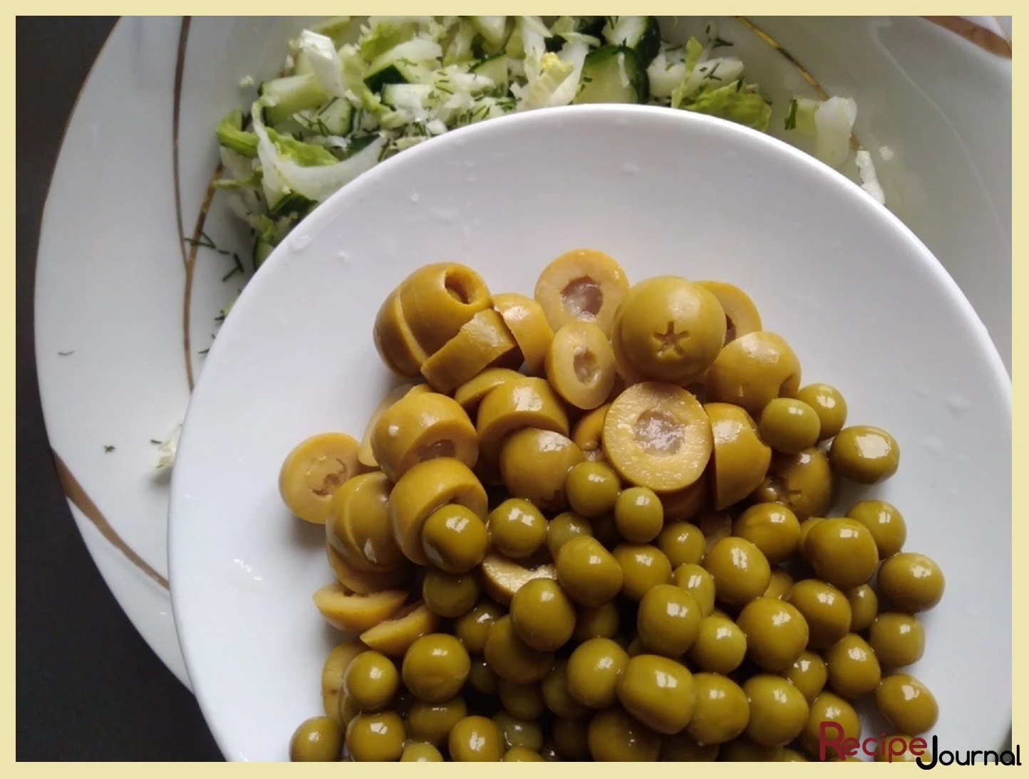Оливки режем колечками и вместе с зеленым консервированным горошком добавляем в салат.